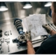 Automotive engineer reviewing vehicle specification documents while examining disassembled car suspension components on workshop table.