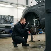 Automotive technician examining car suspension system with wheel removed in professional garage workshop