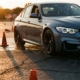 BMW sedan cornering through orange traffic cones on wet asphalt with water spray, golden hour lighting and shadows