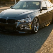 BMW sedan with lowered suspension and exposed chrome coilovers in wheel well cutaway, shot at low angle on asphalt in golden hour lighting.