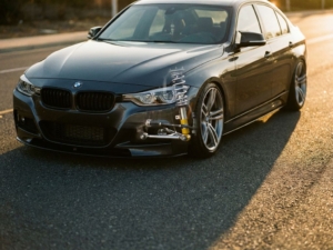 BMW sedan with lowered suspension and exposed chrome coilovers in wheel well cutaway, shot at low angle on asphalt in golden hour lighting.