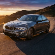 BMW sedan cornering on mountain road with visible suspension components in cutaway wheel well during golden hour