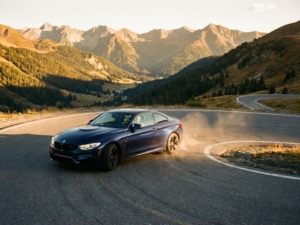 BMW sports car leaning into sharp curve on winding mountain road during golden hour with alpine landscape backdrop
