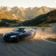 BMW sports car leaning into sharp curve on winding mountain road during golden hour with alpine landscape backdrop