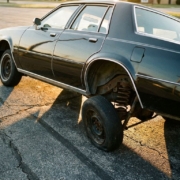 Car with severely compressed suspension leaning at extreme angle on asphalt, chassis nearly touching ground due to suspension failure.
