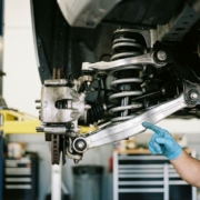 Car suspension system with exposed coil springs and shock absorbers, mechanic's hand pointing to component in garage