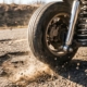 Car wheel and suspension system bouncing over pothole with tire airborne, chrome shock absorber visible, dust flying.