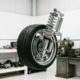 Car wheel and tire suspended by chrome shock absorber and spring system against white automotive workshop background