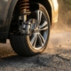 Car wheel cutaway showing shock absorber compressing, coil springs flexing, and brake disc as tire hits raised road surface
