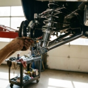 Mechanic adjusting car coilover suspension with wrench on lifted vehicle in professional garage workshop
