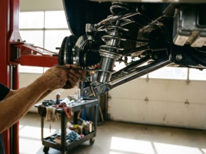 Mechanic adjusting car coilover suspension with wrench on lifted vehicle in professional garage workshop