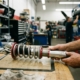 Mechanic inspecting coilover suspension component on workbench, showing detailed spring coils and machined damper assembly