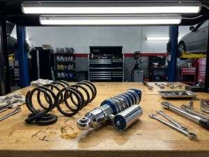 Coilover suspension system and lowering springs on automotive workbench with tools in professional garage setting