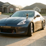 Lowered sports car with modified suspension in suburban driveway, coffee cup on hood, morning sunlight creating shadows.