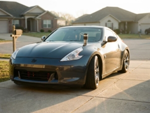 Lowered sports car with modified suspension in suburban driveway, coffee cup on hood, morning sunlight creating shadows.