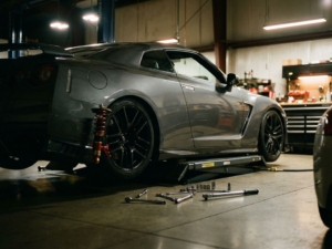 Lowered sports car on hydraulic lift in modern garage showing aftermarket suspension and coilovers with tools on floor