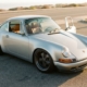 Silver Porsche 911 with lowered stance parked on asphalt, premium leather interior visible through open door, golden hour lighting