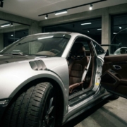 Silver Porsche 911 with open driver door showcasing leather interior and racing harnesses in modern garage