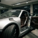 Silver Porsche 911 with open driver door showcasing leather interior and racing harnesses in modern garage