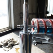 Chrome shock absorber with visible spring coils on automotive workbench under bright workshop lighting with tools