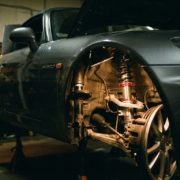Sports car with aftermarket coilover suspension upgrade visible on front wheel, dramatic workshop lighting highlighting metallic components