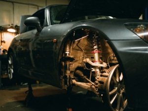 Sports car with aftermarket coilover suspension upgrade visible on front wheel, dramatic workshop lighting highlighting metallic components