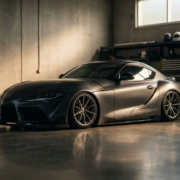 Sports car with lowered suspension and aggressive stance in modern garage with dramatic lighting and polished concrete floor