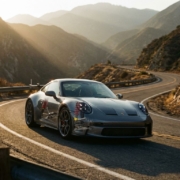 Sports car with visible suspension components navigating sharp mountain curve during golden hour sunset lighting.
