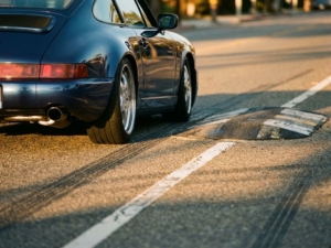Lowered sports car navigating over speed bump with minimal clearance, chrome exhaust visible, golden hour lighting on asphalt road.