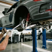 Mechanic adjusting suspension components on sports car lifted in modern automotive garage with LED lighting