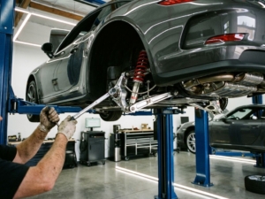Mechanic adjusting suspension components on sports car lifted in modern automotive garage with LED lighting