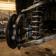 Car wheel suspension system cutaway showing coiled spring wrapped around shock absorber with chrome steel finish in garage