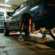 Lowered sports car with compressed suspension and visible shock absorbers in garage with scattered tools around vehicle.