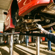 Mechanic pointing to worn suspension components and loose sway bar links on lowered sports car's undercarriage in garage