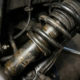 Close-up of lowered car suspension with compressed spring coil around shock absorber showing wear marks in workshop lighting.