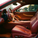 Red sports car interior with premium leather seats, ergonomic steering wheel, and warm ambient lighting from driver's view.