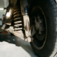 Worn car shock absorber with oil leaks and compressed spring on lowered vehicle's rear wheel suspension system