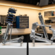 Chrome MacPherson strut and aluminum double wishbone suspension systems displayed on white stands in garage workshop