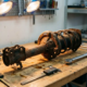 Worn MacPherson strut assembly with rust corrosion and damaged rubber boot on automotive workbench with precision tools