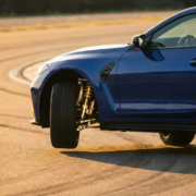 BMW M4 on test track with one wheel lifted during cornering, exposing polished suspension components in golden hour light