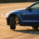BMW M4 on test track with one wheel lifted during cornering, exposing polished suspension components in golden hour light