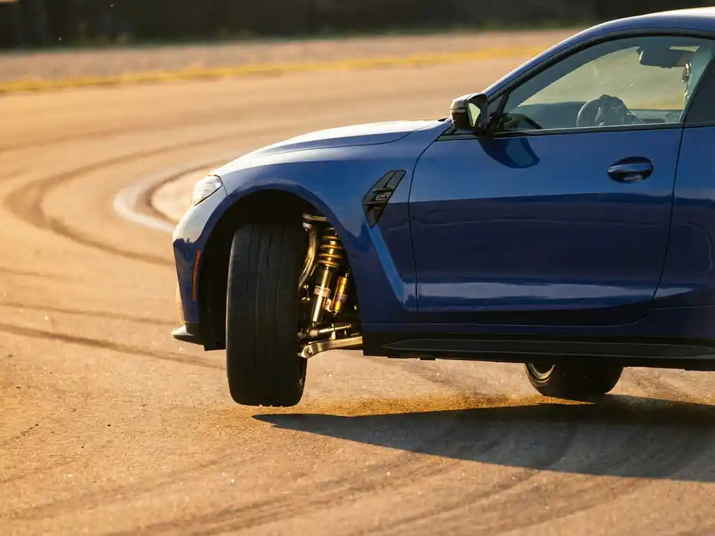 BMW M4 on test track with one wheel lifted during cornering, exposing polished suspension components in golden hour light