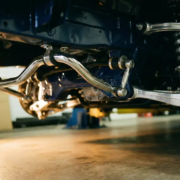 Chrome anti-roll bar with torsional mechanism, mounting bushings and end links beneath sports car chassis in garage lighting