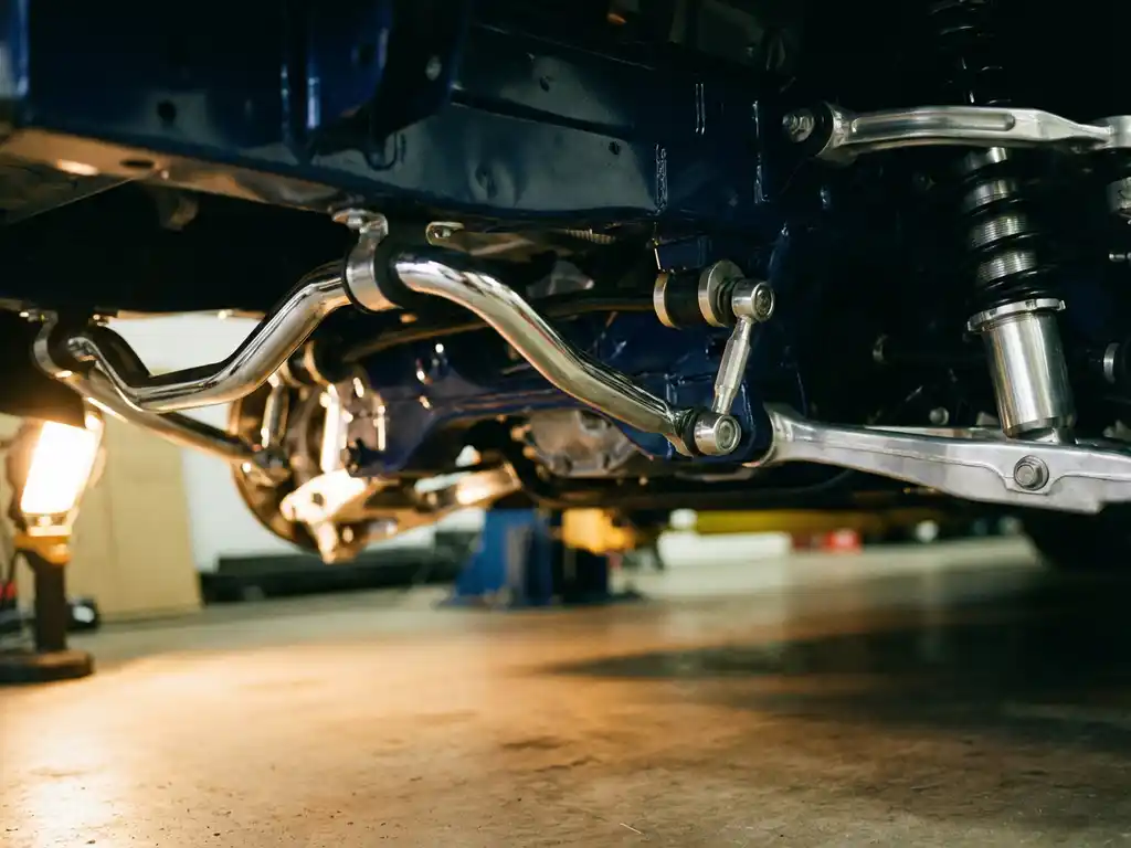 Chrome anti-roll bar with torsional mechanism, mounting bushings and end links beneath sports car chassis in garage lighting