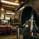 Mechanic installing silver coilovers on lifted sports car in professional garage with precision tools and organized equipment