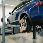 Technician installing chrome coilover suspension components on elevated electric vehicle's rear wheel assembly in modern automotive workshop