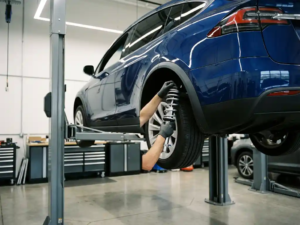 Technician installing chrome coilover suspension components on elevated electric vehicle's rear wheel assembly in modern automotive workshop