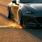 Lowered sports car's front bumper scraping yellow speed bump with sparks flying, dramatic golden hour lighting on asphalt road