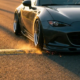 Lowered sports car's front bumper scraping yellow speed bump with sparks flying, dramatic golden hour lighting on asphalt road