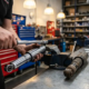 Mechanic's hands adjusting chrome shock absorber with specialized tools on workbench, worn replacement part nearby in professional automotive workshop